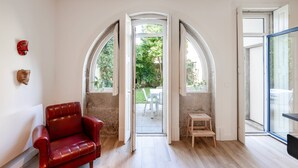 Interior con una butaca de cuero rojo, un taburete de madera y vistas a un patio exterior por una puerta abierta.