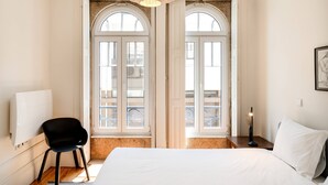 Un dormitorio con cama, una silla, una mesita de noche y ventana con vista a un balcón.
