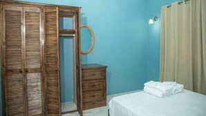 A bedroom with a wooden wardrobe, a bedside table, a bed with white linens, and a curtain. - Lovely entire new 2 Bedroom Apartment in Corinth (Gros Islet Castries)