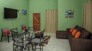 A living room with a glass dining table, brown sofa, and a television mounted on the wall. - Lovely entire new 2 Bedroom Apartment in Corinth (Gros Islet Castries)