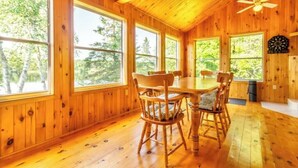A wooden cabin with large windows, a dining table, and chairs. - Jack's Lake Retreat - Perfect for multi-families! (Golden Valley)