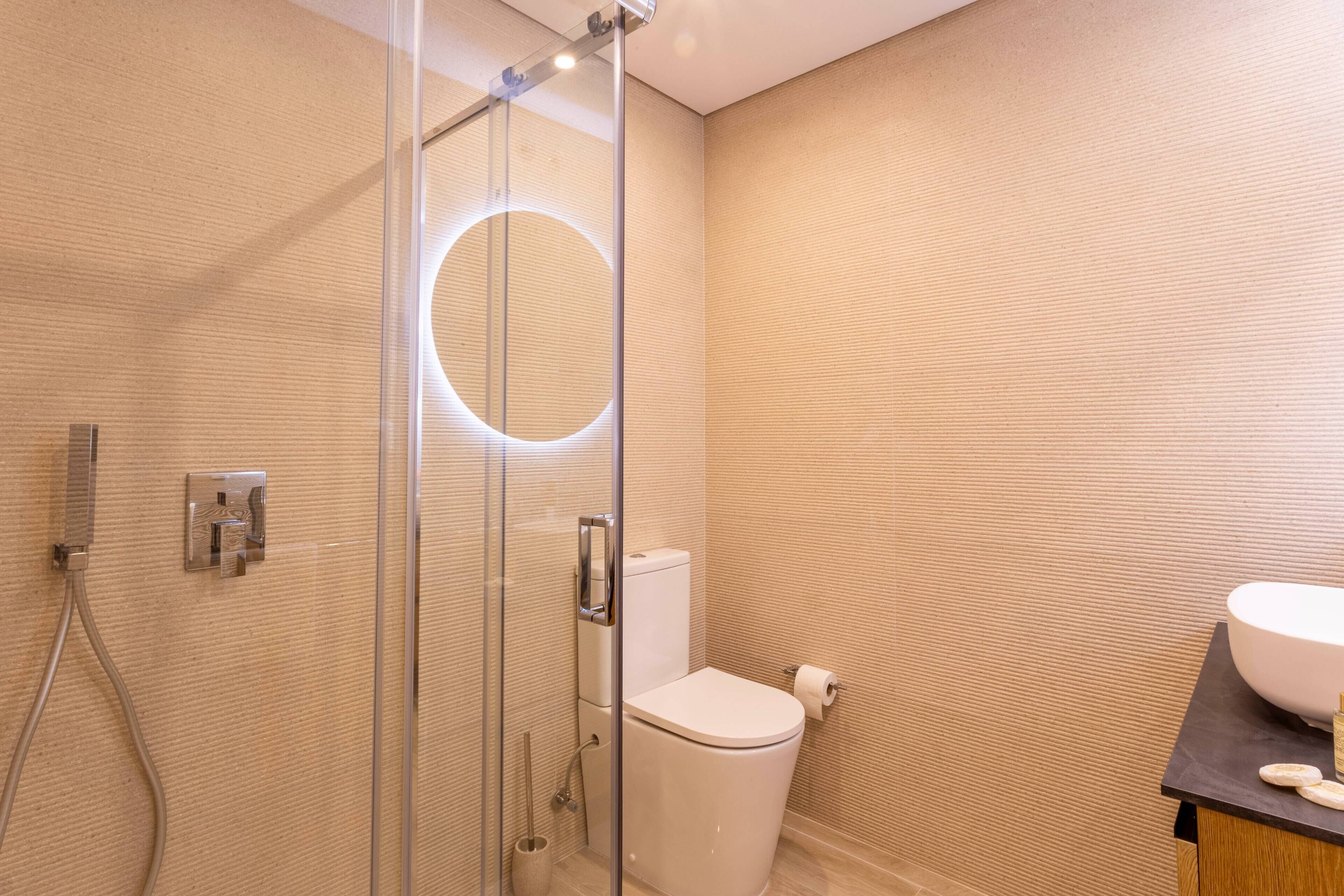 A modern bathroom with a glass shower enclosure, a toilet, and a sink with a large basin.