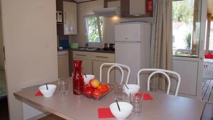 A compact kitchen with a dining area, featuring a refrigerator, microwave, and a small dining table with chairs. - ZEcamping 4* 500m plage parc aquatique dog friendly locatif TV clim (Hyères)