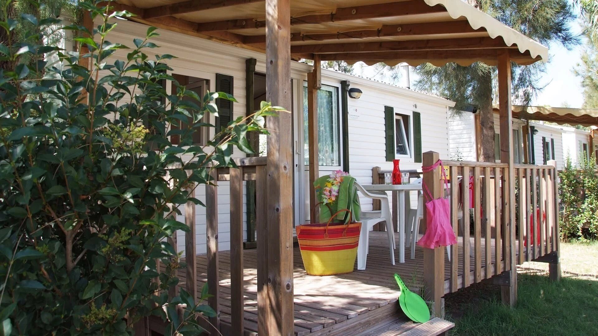 A wooden deck with a covered porch, a table with chairs, and a small garden area with a potted plant and a shovel.