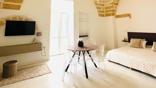 Ein geräumiges Schlafzimmer mit Backstein-Decke, einem Bett, einem Fernseher und einem Essbereich mit Stühlen und einem Tisch.