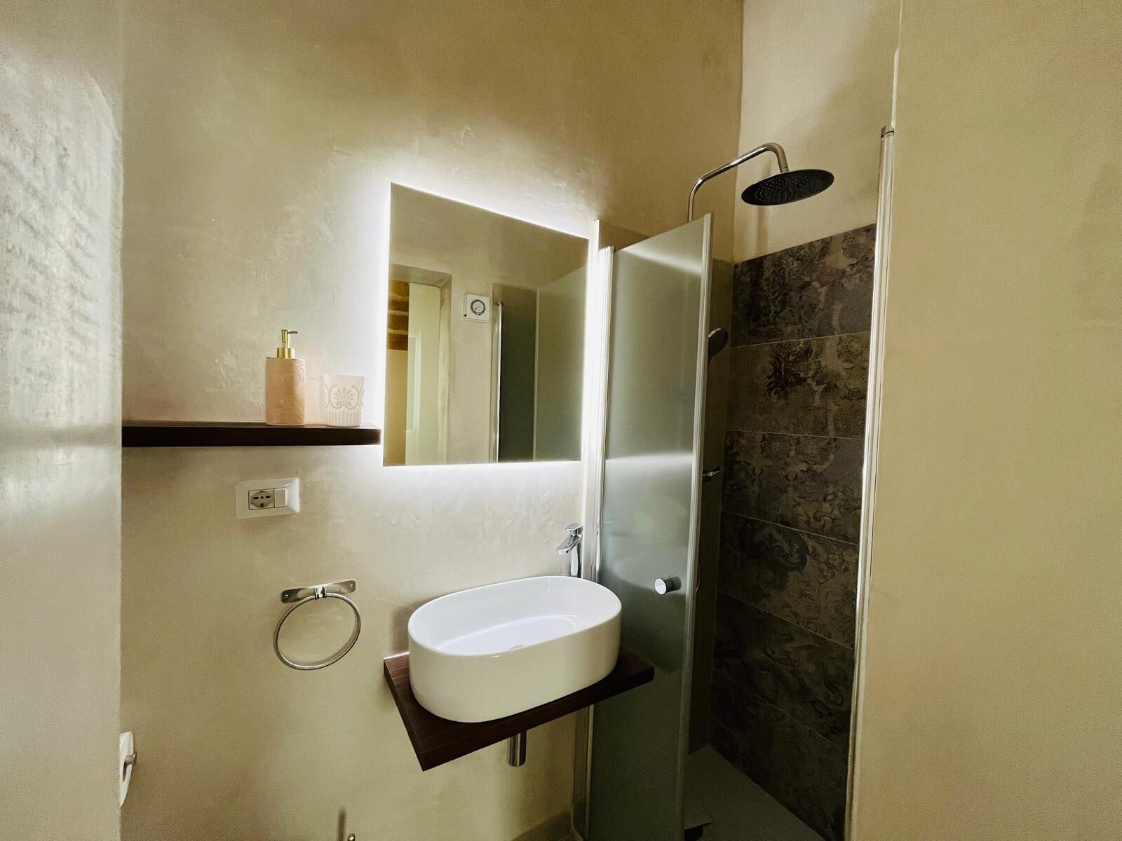 A bathroom with a white sink, a mirror, a shower, and a towel rack.
