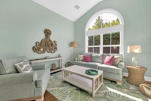 A living room with a sofa, a coffee table, and a window with a view of greenery.