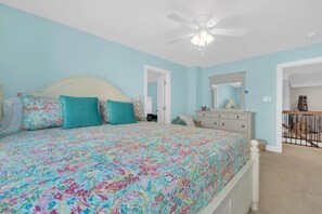 A bedroom with a bed, a dresser, a ceiling fan, and a door leading to another room.