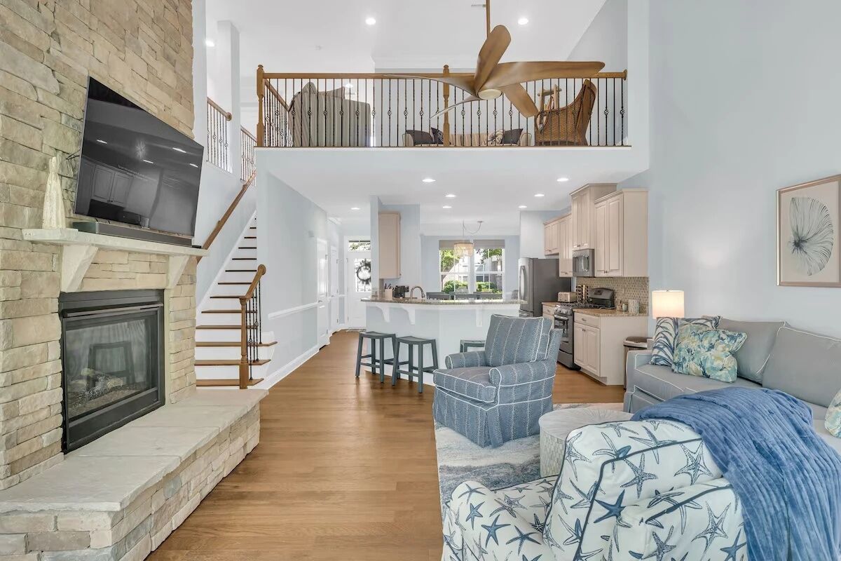 A spacious living area with a fireplace, a staircase leading to an upper level, and a kitchen in the background.