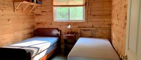 Una pequeña cabaña con dos camas individuales, una ventana con vistas a la vegetación y un interior de madera.