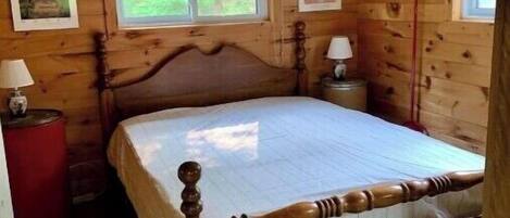 A wooden cabin bedroom with a bed, two bedside tables, a window, and a door.