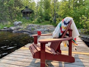 Eine Holzsteg mit einem roten Adirondack-Sessel und einer roten Tasse darauf.