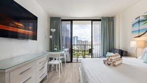 Una moderna camera d'albergo con un letto grande, una scrivania con sedie, un balcone con vista sulla città e un quadro appeso al muro.