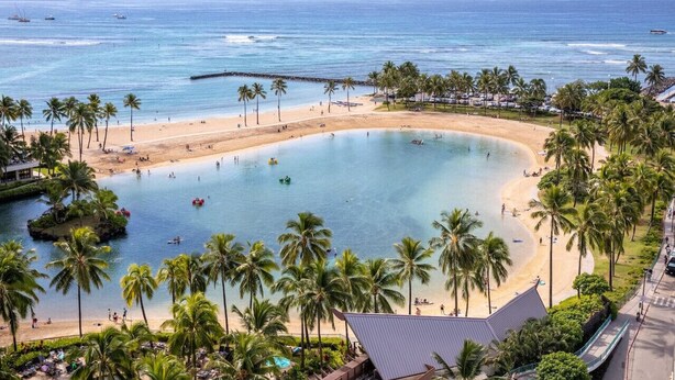 Un resort sulla spiaggia con una grande piscina, palme e vista sull'oceano.