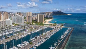 Una marina con numerose imbarcazioni ormeggiate, uno skyline con grattacieli e una spiaggia con una montagna sullo sfondo.