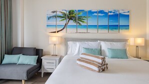 Una camera d'albergo con un letto, un comodino, una sedia e un quadro raffigurante una spiaggia.