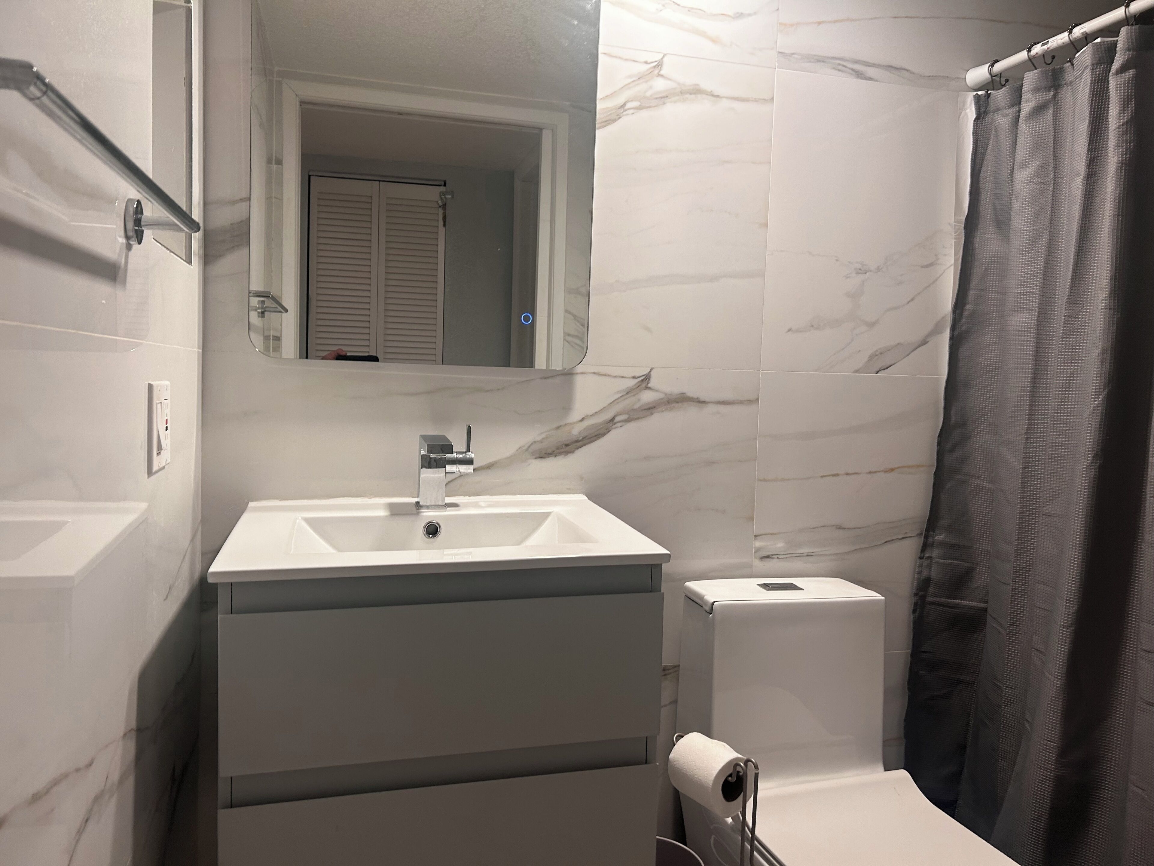Een badkamer met een wit wastafelmeubel, spiegel en douchegordijn.