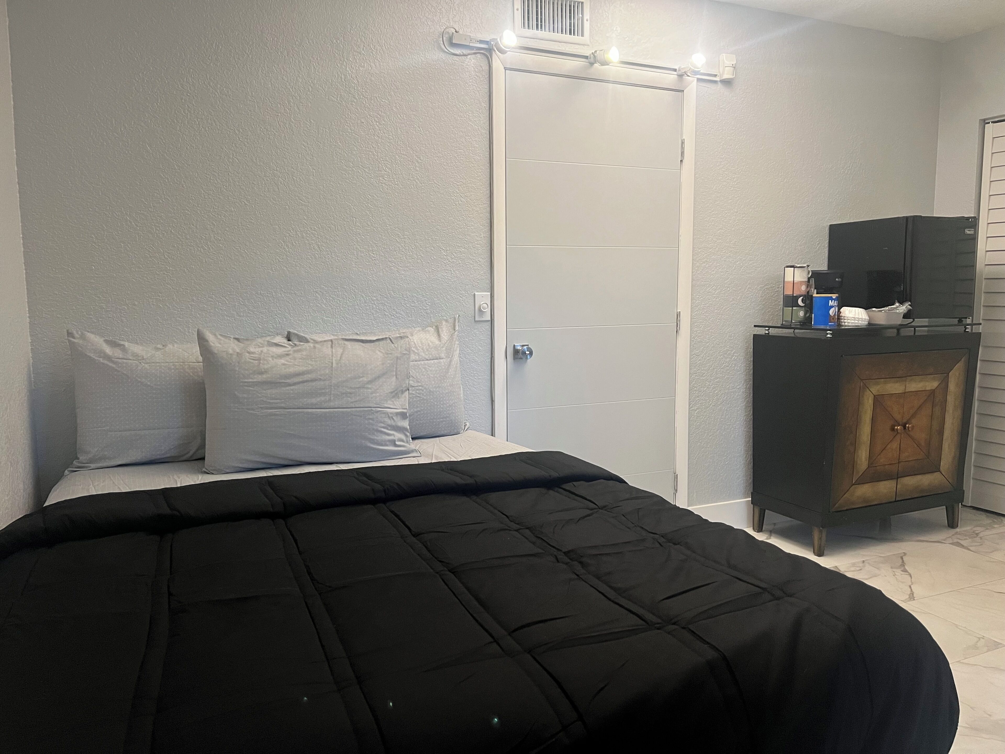 A bedroom with a bed, pillows, a wardrobe, and a small cabinet with items on top.