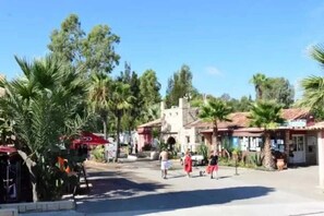 A street scene with palm trees, a building with a red awning, and a few people walking.