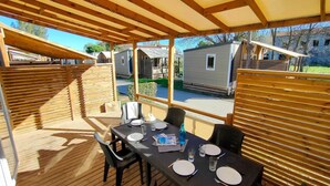 A covered outdoor dining area with a table set for two, surrounded by wooden railings, overlooking a row of mobile homes.