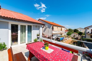 Un balcón con mesa y sillas, una planta en maceta y vistas a casas vecinas.