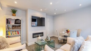Una sala de estar moderna con chimenea, televisor de pantalla plana, estantería y comedor con sillas.
