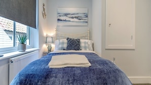 Un dormitorio con cama, ventana con planta, radiador, lámpara de pared y un cuadro.
