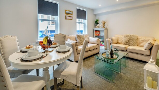 Un salón moderno con una mesa de comedor preparada para cuatro personas, un sofá y una mesa de centro de vidrio.