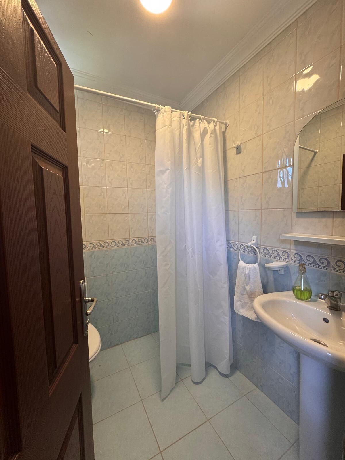 A bathroom with a toilet, a sink, a shower curtain, and a mirror.