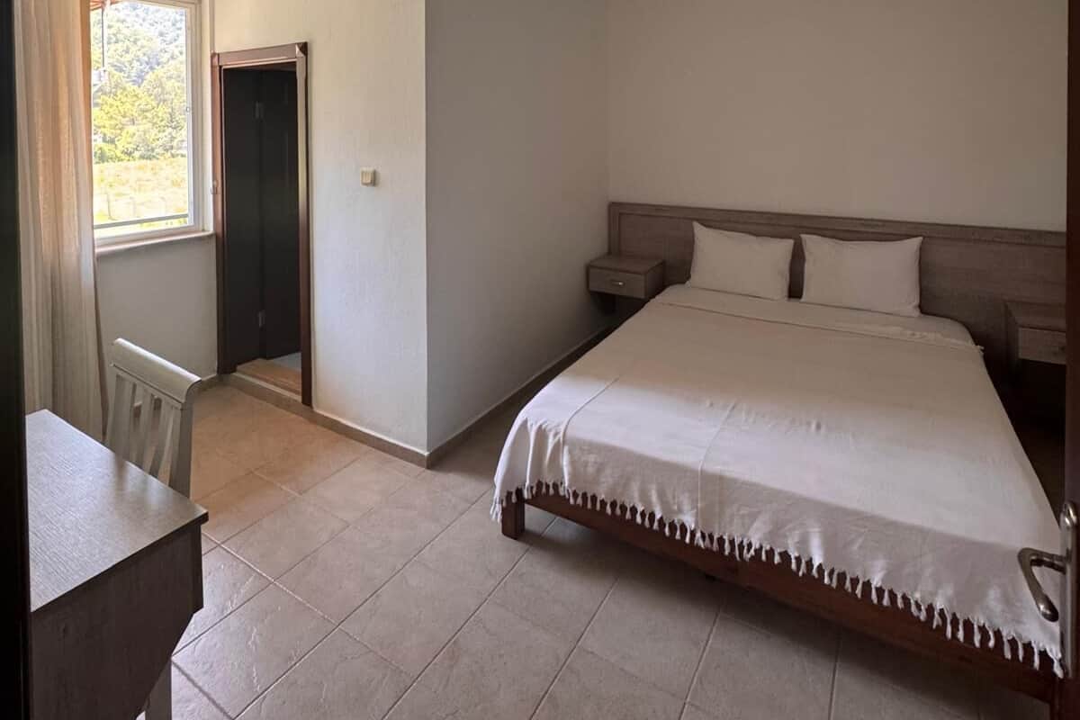 Un dormitorio con cama, mesitas de noche, un escritorio y una ventana.