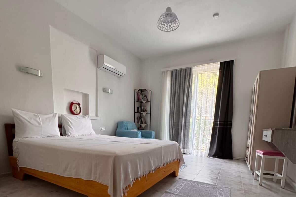 Un dormitorio con cama, un escritorio pequeño, una silla, una estantería y una ventana con cortinas.