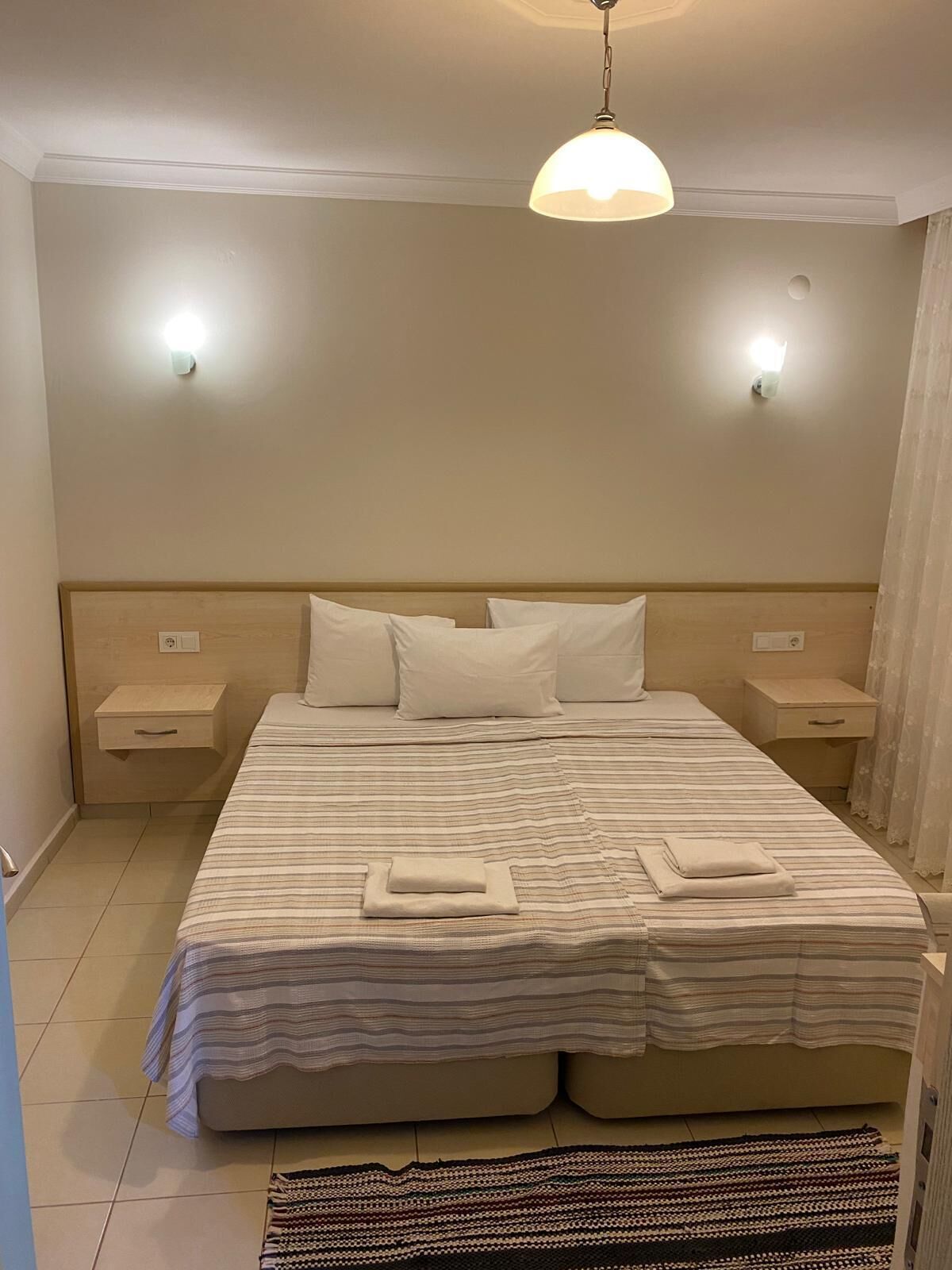 A neatly arranged bedroom with a large bed, two bedside tables, a hanging light fixture, and a patterned rug.
