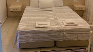 A neatly arranged bedroom with a large bed, two bedside tables, a hanging light fixture, and a patterned rug.