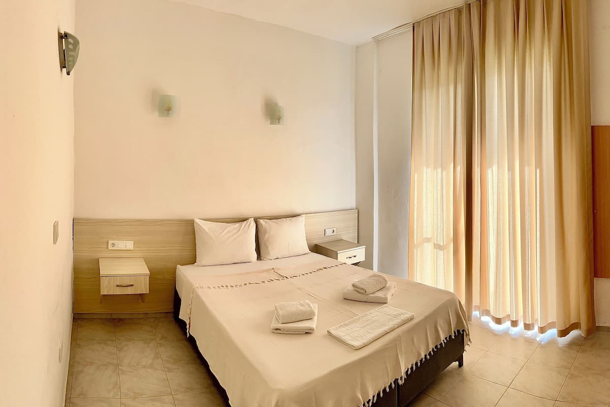 Habitación de hotel con cama, mesitas de noche, armario y ventana con cortinas.