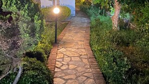 A stone pathway leading to a building with a modern design, surrounded by well-maintained greenery and illuminated by street lamps. - MERMAID PANSIYON (Marmaris)