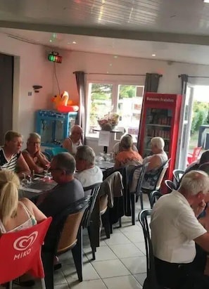 A restaurant with patrons seated at tables, a visible menu stand, and a view of the outside through the window.