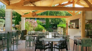 Un patio al aire libre con vigas de madera, sillas de metal verde y mesas.