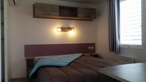 Un dormitorio con cama, mesitas de noche, una lámpara de pared, una ventana con cortinas y un estante empotrado sobre la cama.