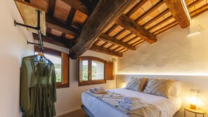 Une chambre à coucher avec un lit, des poutres en bois, une fenêtre et un vêtement suspendu.