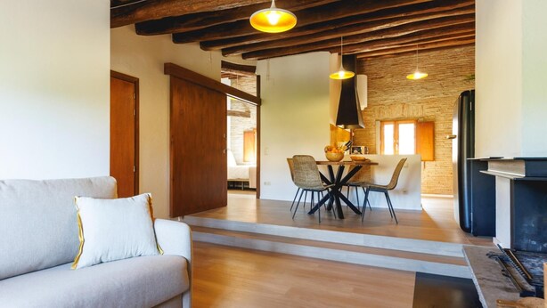 Un salon moderne avec un canapé, une table à manger et des chaises. On aperçoit une cheminée et un coin cuisine à l’arrière-plan.