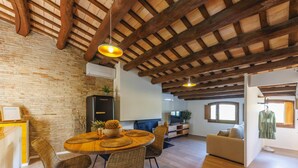 Un grand espace de vie doté d’un plafond en bois, d’une table à manger avec des chaises, d’un téléviseur et d’un canapé.