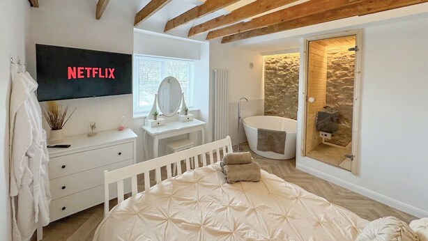 A bedroom with a bed, a vanity with a mirror, a TV displaying 'NETFLIX', and a stone wall in the bathroom. - 2 bedroom accommodation in Stanhope, near Bishop Auckland (Stanhope, near Bishop Auckland)