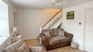 A living room with a brown sofa, a plaid armchair, a small table with a lamp, and a staircase. - 2 bedroom accommodation in Stanhope, near Bishop Auckland (Stanhope, near Bishop Auckland)