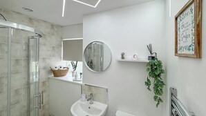 A modern bathroom with a glass shower enclosure, a white sink, a round mirror, and a toilet. There is a shelf with toiletries and a framed inspirational quote on the wall. - 2 bedroom accommodation in Stanhope, near Bishop Auckland (Stanhope, near Bishop Auckland)