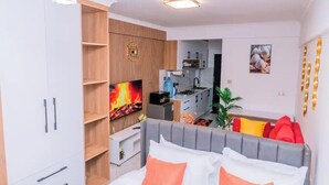A modern bedroom with a grey headboard, white bedding, and a TV displaying a fireplace. - Skyview loft retreat Apartment, Smarthome Yaya (Nairobi)