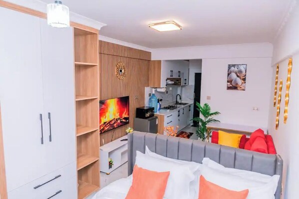 Une chambre moderne avec une tête de lit grise, du linge de lit blanc et un téléviseur diffusant une image de cheminée.