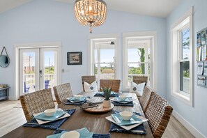 A dining area with a round table, wicker chairs, and a chandelier.