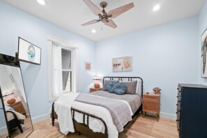 A bedroom with a bed, a ceiling fan, a dresser, a nightstand, and a mirror.