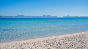 Uma praia com águas turquesa cristalinas e montanhas distantes sob um céu azul límpido.