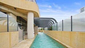 A swimming pool with a curved roof structure, surrounded by a high fence and beige walls. - Broadbeach Elegant apartment with views! (Broadbeach)